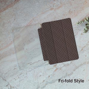 May include: A clear plastic case and a brown tri-fold style cover with white polka dots. The text "Fri-fold Style" is visible in the lower right corner. The items are displayed on a marble surface.