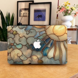 Puede incluir: Una funda para portátil con un diseño de vidriera que representa un sol y nubes. La funda tiene un logotipo blanco de Apple. El diseño incorpora tonos azules, amarillos y marrones, creando un aspecto vibrante y artístico.