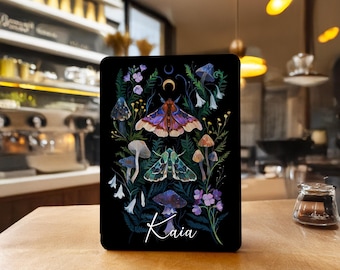 May include: Black tablet case with a vibrant illustration of moths, mushrooms, and flowers. The design incorporates a crescent moon and the name "Kaia" in a script font. The artwork is set against a dark background.