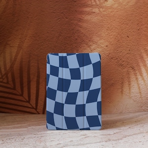 May include: A tablet case featuring a blue and light blue checkered pattern. The case is positioned upright against a textured brown backdrop. The design has a wavy, distorted checkerboard appearance.