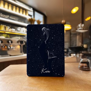 Op de afbeelding: Een rechthoekig, donkerblauw decoratief item met een witte illustratie van een walvishaai en een manta rog tegen een sterrenachtergrond. Het woord "Kaia" staat in witte letters onderaan.