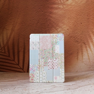 Könnte beinhalten: Eine Tablet-Hülle mit Patchwork-Design. Die Hülle zeigt eine Mischung aus floralen und geometrischen Mustern in Pastelltönen von Rosa, Blau und Weiß. Die Hülle ist für ein Tablet konzipiert und bietet Schutz mit einem dekorativen Aussehen.