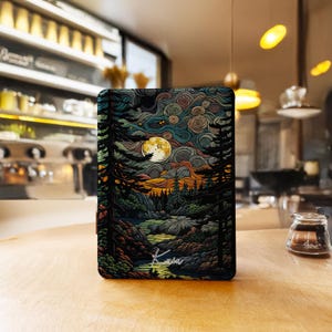 Può includere: Una custodia rettangolare con una vivace illustrazione di una scena di foresta illuminata dalla luna. L'opera d'arte presenta una luna piena, un fiume e alberi sagomati in tonalità di verde, blu, arancione e nero. La custodia ha il nome "Karin" in scrittura bianca.