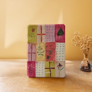May include: A rectangular, colorful tin box with a patchwork design featuring floral and leaf illustrations. The box has a variety of colors, including pink, green, and yellow. The box is sitting on a wooden surface.