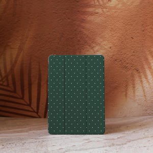 May include: A dark green tablet case with a white polka dot pattern. The case is standing upright against a textured brown background. The case is designed to protect a tablet.