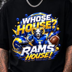 Pode incluir: Uma t-shirt preta com uma estampa gráfica com o texto WHOSE HOUSE? RAMS HOUSE! O design inclui um jogador de futebol americano com cabeça de carneiro, um capacete azul e amarelo e uma bola de futebol americano castanha sobre fundo azul.