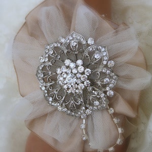 May include: A delicate ivory tulle flower with a silver rhinestone brooch in the centre. The brooch has a floral design with intricate details.