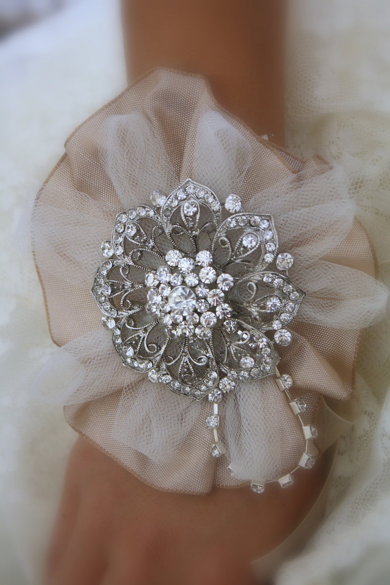 May include: A delicate ivory tulle flower with a silver rhinestone brooch in the centre. The brooch has a floral design with intricate details.
