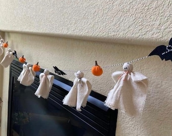 May include: A Halloween garland with white felt ghosts, orange felt pumpkins, and black felt bats. The garland is strung on a white twine and is hanging from a fireplace mantel.