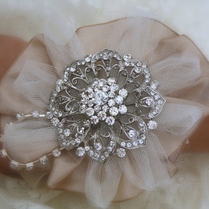 May include: A delicate white tulle flower with a silver rhinestone brooch in the centre. The brooch is a floral design with intricate details and sparkling rhinestones.