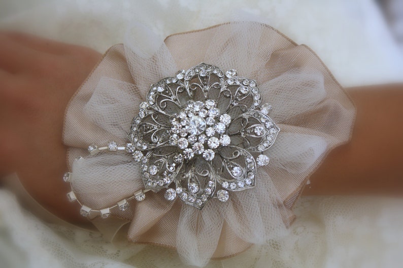May include: A delicate white tulle flower with a silver rhinestone brooch in the centre. The brooch is a floral design with intricate details and sparkling rhinestones.