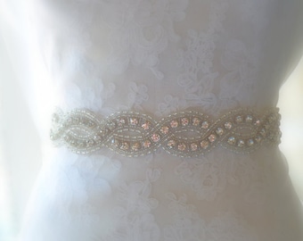 May include: A white beaded bridal belt with clear iridescent rhinestones. The belt is designed with a wavy pattern and is perfect for adding a touch of sparkle to a wedding dress.