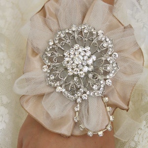 May include: A delicate ivory and beige tulle flower with a silver rhinestone brooch. The brooch features a floral design with intricate details and sparkling rhinestones.