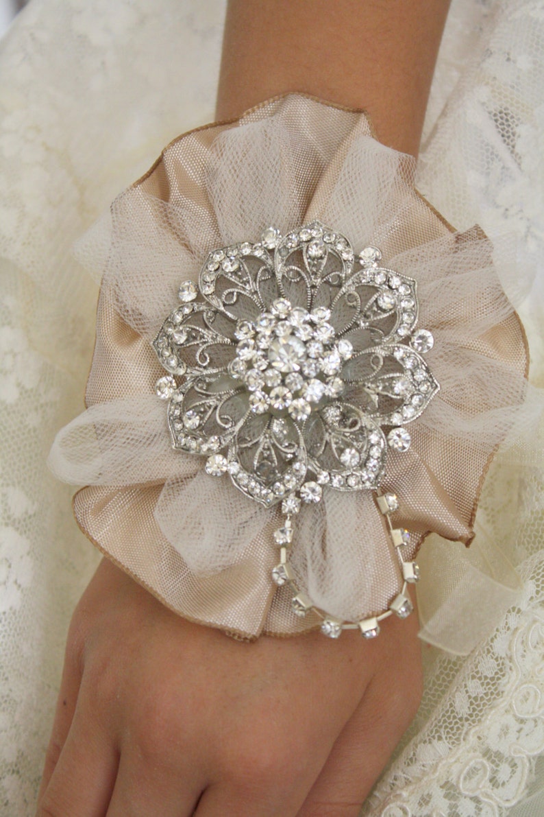 May include: A delicate ivory and beige tulle flower with a silver rhinestone brooch. The brooch features a floral design with intricate details and sparkling rhinestones.