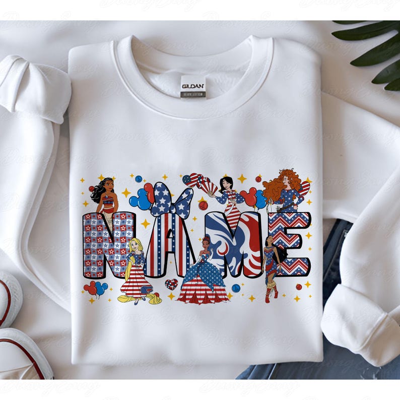 K&ouml;nnte beinhalten: Wei&szlig;es Sweatshirt mit einem patriotischen Design mit dem Wort "NAME" in Rot, Wei&szlig; und Blau. Die Buchstaben sind mit Sternen, Streifen und Cartoonfiguren verziert. Rote und blaue Luftballons sind ebenfalls enthalten.