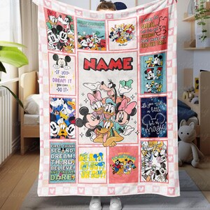 Könnte beinhalten: Eine große, rechteckige Disney-Decke mit verschiedenen Zeichentrickfiguren und Zitaten. Die Decke ist hauptsächlich rosa und weiß, mit mehreren quadratischen Feldern mit Micky Maus, Minnie Maus und anderen Figuren. Das Wort "NAME" ist prominent dargestellt.