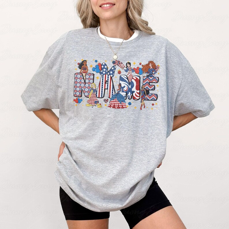 K&ouml;nnte beinhalten: Ein graues Sweatshirt mit dem Wort "NAME" in einem patriotischen Design. Die Buchstaben sind mit Illustrationen von Frauen in rot, wei&szlig; und blau gekleidet, mit Sternen und Streifen gef&uuml;llt. Das Sweatshirt hat einen Rundhalsausschnitt und lange &Auml;rmel.