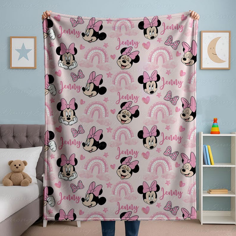 May include: Pink fleece blanket with a repeating pattern of Minnie Mouse faces, bows, rainbows, and the name "Jenny". This soft blanket is ideal for a child's bedroom or nursery, offering warmth and comfort.