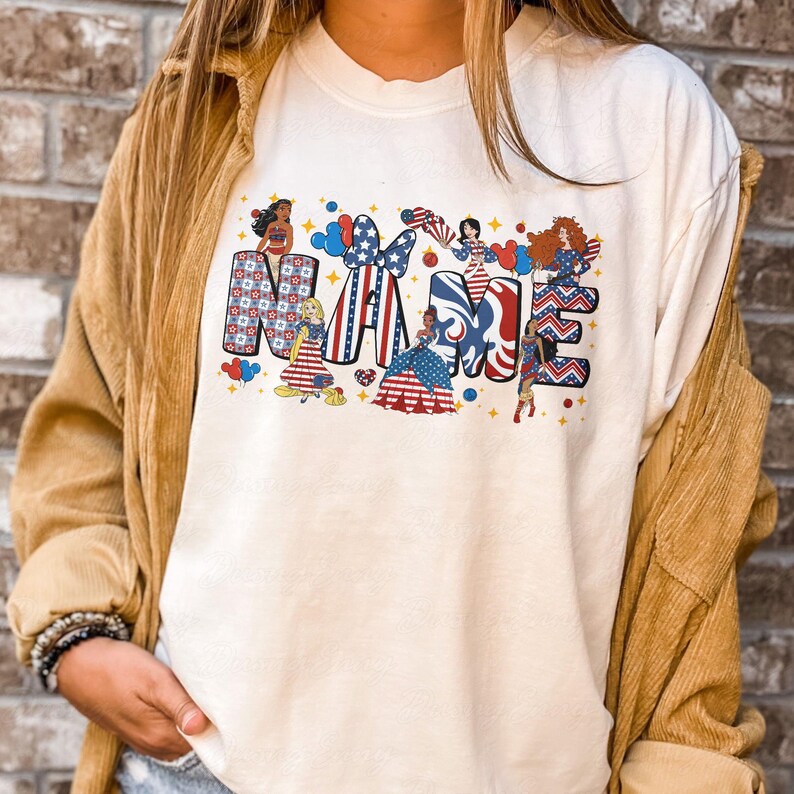 K&ouml;nnte beinhalten: Cremefarbenes T-Shirt mit dem Wort "MAMA" in einem patriotischen Design. Jeder Buchstabe ist mit Mustern und Illustrationen von Frauen in rot, wei&szlig; und blauen Kleidern mit Sternen und Streifen verziert.