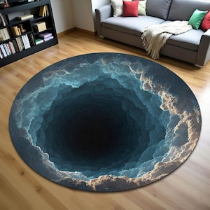 May include: A round area rug with a 3D cloud design. The rug features a dark blue center that fades into lighter shades of blue and white, creating a visual depth effect. The rug is placed on a wooden floor.