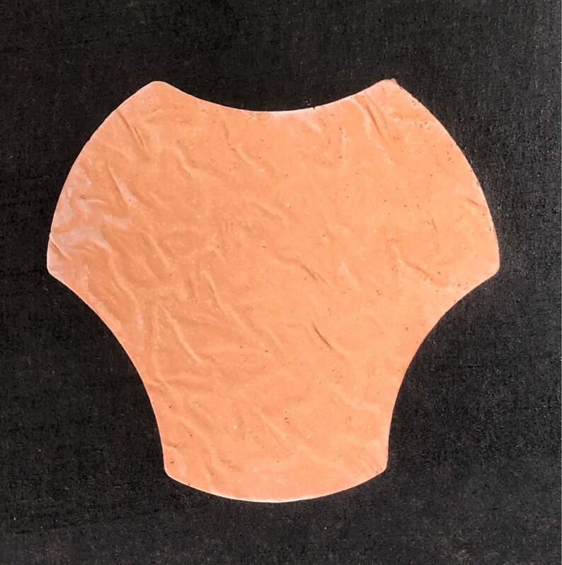 Pode incluir: Um bloco de pavimenta&ccedil;&atilde;o de concreto cor de p&ecirc;ssego com um formato org&acirc;nico &uacute;nico. O bloco tem uma superf&iacute;cie texturizada e uma borda ligeiramente arredondada.