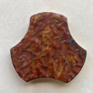 Pode incluir: Um azulejo de cer&acirc;mica vermelho e dourado com um padr&atilde;o abstrato &uacute;nico. O azulejo tem a forma de um tri&acirc;ngulo arredondado com tr&ecirc;s pontas.