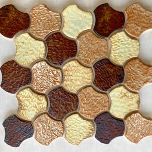 May include: A sheet of brown, beige, and cream ceramic tile with a textured surface. The tiles are shaped like rounded hexagons and are arranged in a repeating pattern.