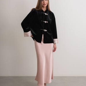 May include: A black velvet jacket with floral button closures and light pink trim on the sleeves. Paired with a long, light pink satin skirt. The outfit is completed with black pointed-toe heels.