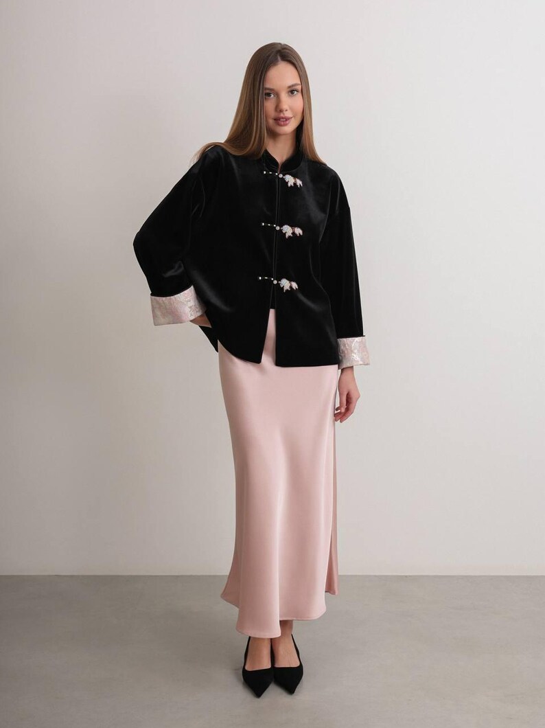 May include: A black velvet jacket with floral button closures and light pink trim on the sleeves. Paired with a long, light pink satin skirt. The outfit is completed with black pointed-toe heels.