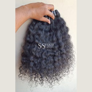Op de afbeelding: Een bundel donkerbruine, golvende hairextensions met een weft aan de bovenkant. Het haar heeft een natuurlijke, volumineuze textuur met gedefinieerde krullen. De tekst SS HAIR EXPORT staat in het wit in het midden van de haarbundel.