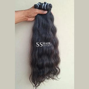 Pu&ograve; includere: Un fascio di capelli scuri e ondulati tenuto in mano. I capelli sono di un nero intenso con onde naturali. Il testo "SS HAIR EXPORT" &egrave; visibile.