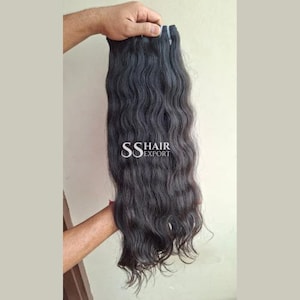 Pu&ograve; includere: Extension di capelli ondulati scuri tenute in mano. I capelli sono di un nero intenso con un motivo ondulato naturale. Il testo "SS HAIR EXPORT" &egrave; visibile sui capelli.