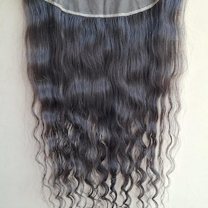 以下が含まれることがあります： ダークウェーブヘアレースフロントウィッグ。ウィッグは、透け感のあるレースベースと、長く濃いウェーブヘアが特徴です。髪は深みのある自然な黒色で、わずかな光沢があります。ウィッグは手で持たれています。