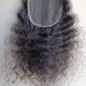 以下が含まれることがあります： 上部に細かい半透明のレースベースを備えたダークブラウンのヘアクロージャーピース。髪はレースから下に向かって流れる深いウェーブのかかった質感で、自然な見た目のルーズなカールがボリューム感のある外観を作り出しています。