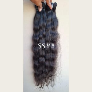 Könnte beinhalten: Ein Bündel langer, dunkelbrauner, welliger Haarverlängerungen, das oben gehalten wird. Das Haar hat eine natürliche Textur und einen leichten Glanz. Der Text SS HAIR EXPORT ist in Weiß in der Mitte des Haarbündels aufgedruckt.