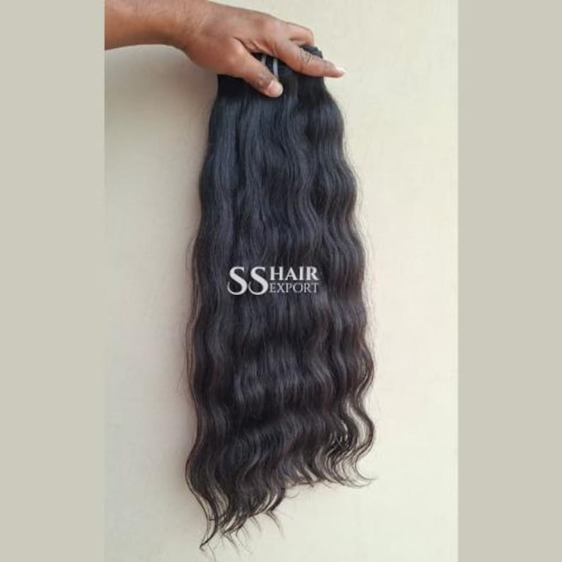 Pu&ograve; includere: Un fascio di capelli scuri e ondulati tenuto in mano. I capelli sono di un nero intenso con onde dall'aspetto naturale. Il testo "SS HAIR EXPORT" &egrave; visibile nell'immagine.