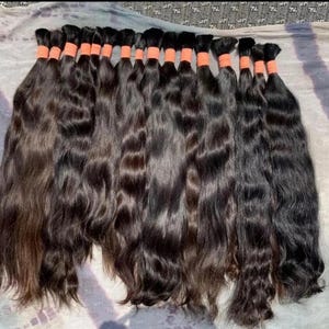 Può includere: Una collezione di quattordici ciocche di capelli umani lunghi, dal castano scuro al nero. Ogni ciocca è fissata nella parte superiore con un elastico arancione brillante, mantenendo le ciocche ondulate e fluide allineate in modo uniforme.