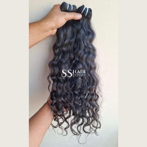 May include: A bundle of long, dark, wavy hair extensions with a natural texture. The hair is secured at the top with a thick, dark band. The text SS HAIR EXPORT is printed in white in the centre of the hair bundle, indicating the brand name.