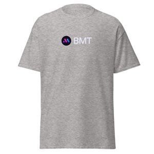 May include: A grey t-shirt with a black circle containing a purple and blue stylised letter M and the text "BMT" in white.