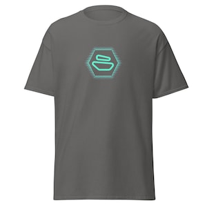 Op de afbeelding: Een donkergrijs T-shirt met een turquoise geometrisch logo in het midden. Het logo is een hexagon met een gestileerde afbeelding van drie gestapelde vormen.