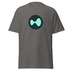 May include: A gray t-shirt featuring a teal and dark teal abstract design. The design is a circle with a teal shape inside. The t-shirt has short sleeves and a crew neck.