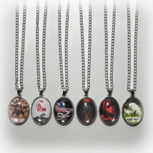 May include: Seven silver chain necklaces with round glass pendants featuring different images from the Resident Evil video game series. The pendants feature images of characters, monsters, and logos from the games.