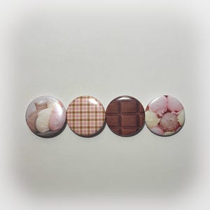 May include: Four round pinback buttons with different designs. One button features a knitted design with pink and white elements. Another has a pink and brown plaid pattern. A third button shows a chocolate bar. The last button displays scoops of ice cream.