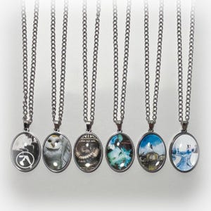 May include: Seven silver chains with round glass pendants featuring album covers. The pendants feature images of a white owl, a band with a black and white logo, a band with a black and white logo, a band with a black and white logo, a band with a black and white logo, a band with a black and white logo, and a snowy landscape.