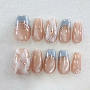 May include: A set of ten artificial nails in various designs. Some nails feature a light blue tip, others have a light pink base with a silver crisscross pattern. The nails are oval-shaped and have a glossy finish.
