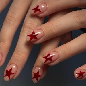 Pode incluir: Close-up de mãos com unhas cor de pele com arte de unhas de estrela vermelha.