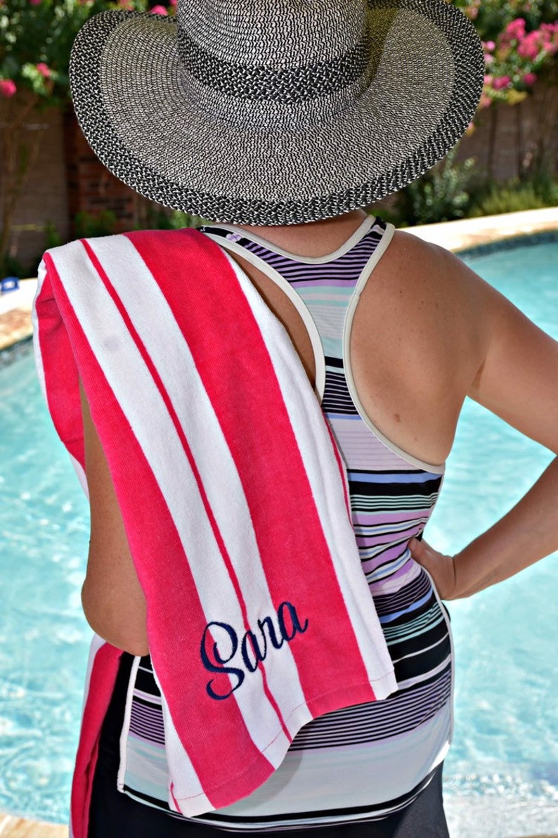 Adult woman holding a personalized hot pink beach towel with name embroidered on the end of the towel.  The name is in cursive embroidery thread in navy on a hot pink towel.