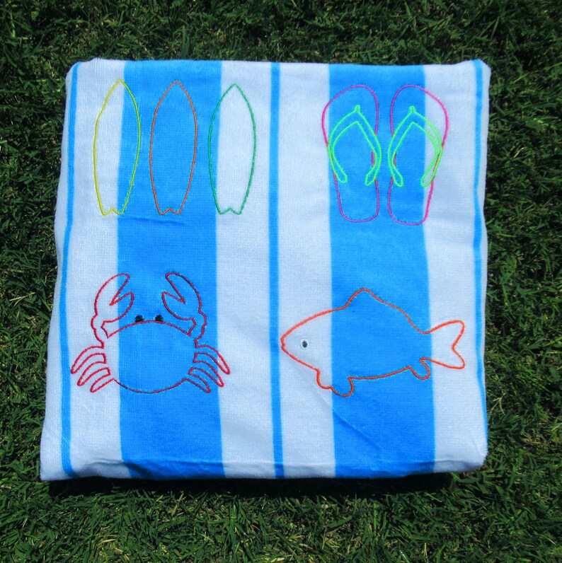 Puede incluir: Una toalla de playa a rayas azules y blancas con dise&ntilde;os bordados. La toalla presenta im&aacute;genes de tablas de surf, chanclas, un cangrejo y un pez. Los detalles bordados son de varios colores, incluyendo rojo, verde y naranja.