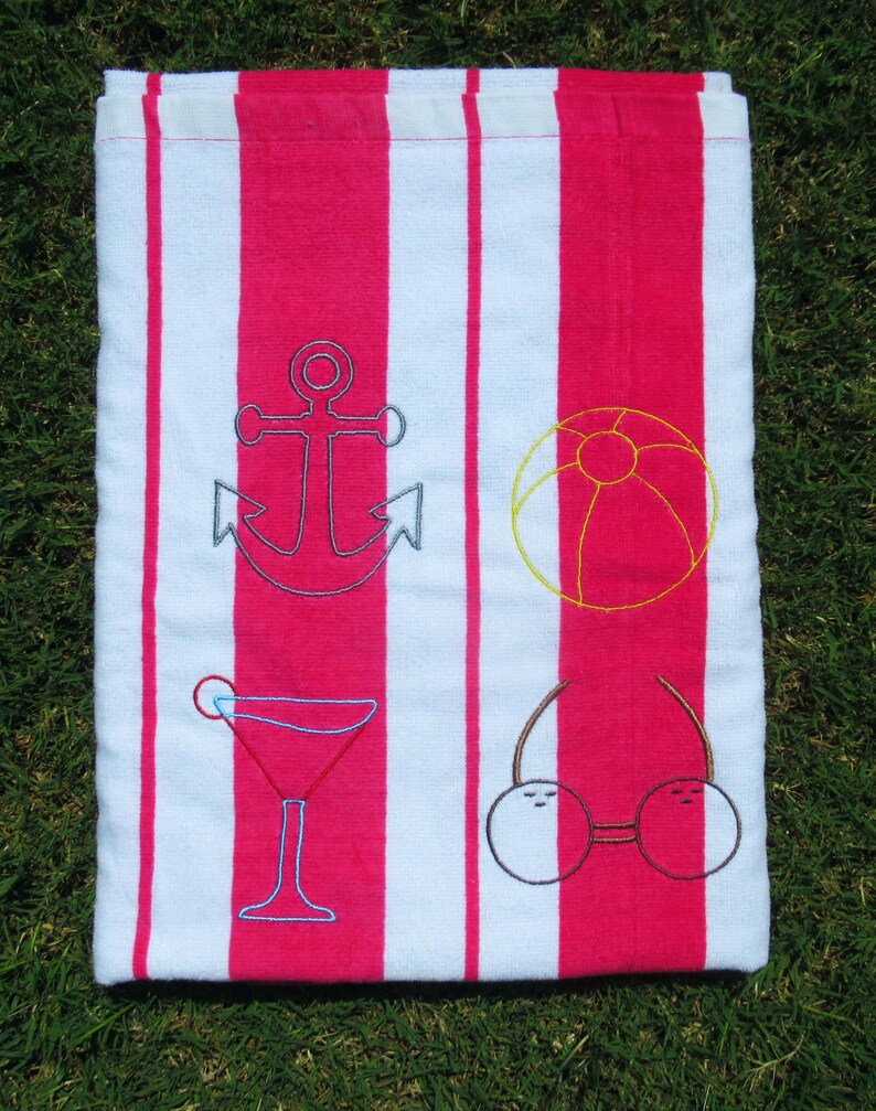 Puede incluir: Una toalla de playa con rayas verticales alternas blancas y rosa brillante. Bordados en la toalla hay un ancla azul, un bal&oacute;n de playa amarillo, un c&oacute;ctel rojo y unas gafas de sol con cerezas.