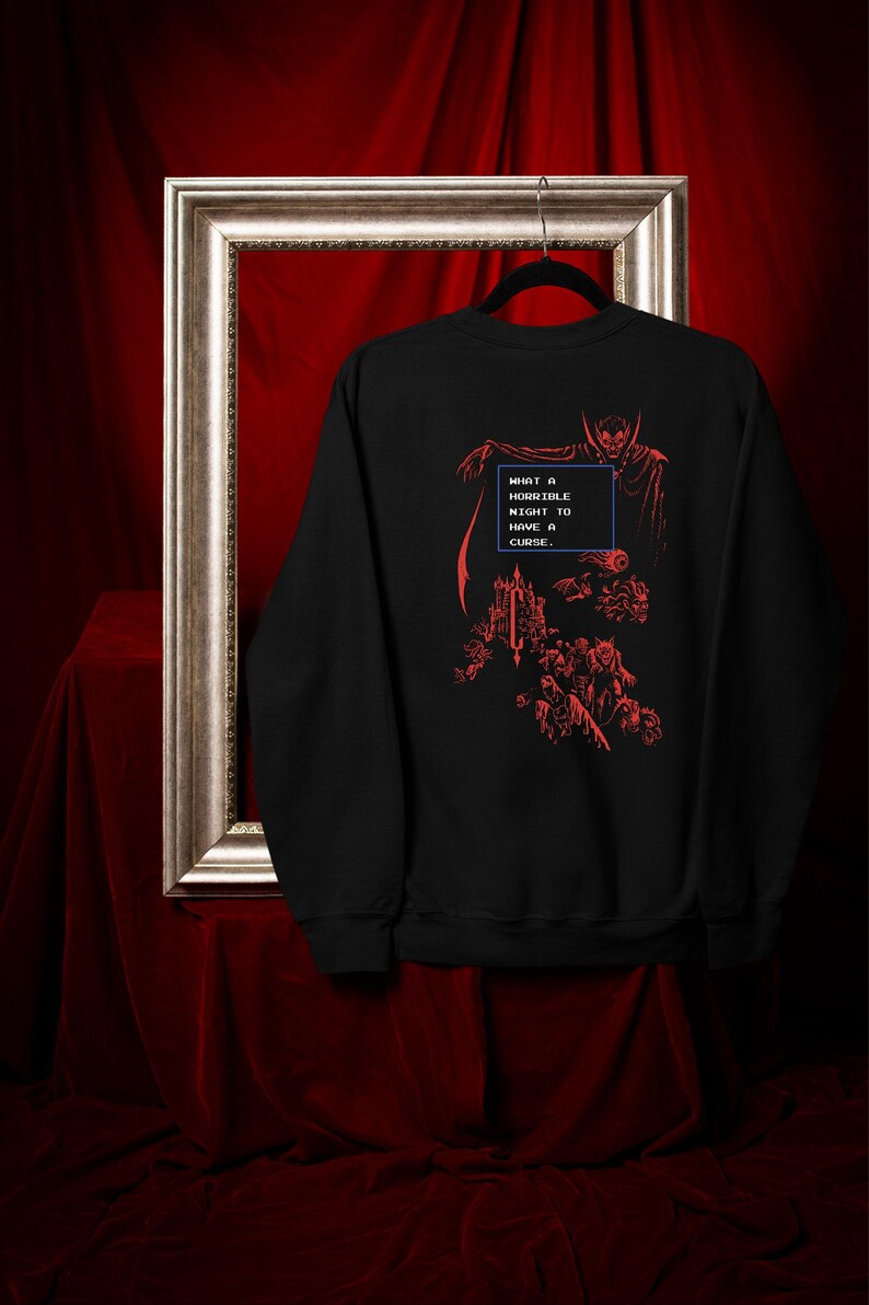 May include: Black sweatshirt with a red graphic design featuring a vampire, castle, and the text "WHAT A HORRIBLE NIGHT TO HAVE A CURSE." The design is reminiscent of a retro video game aesthetic. The sweatshirt is displayed on a hanger.